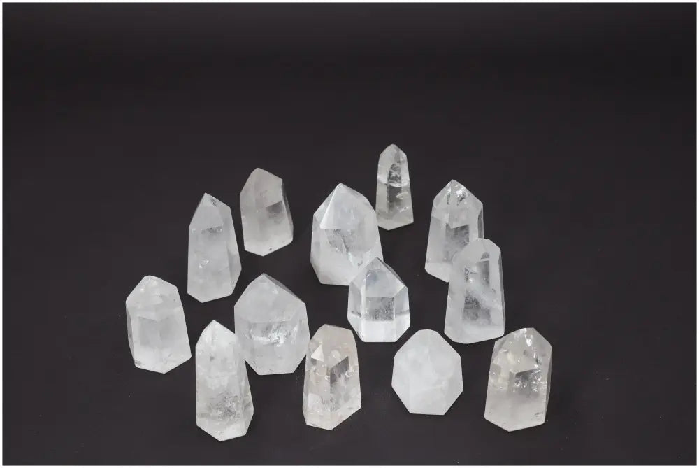 Collection of twelve clear quartz obelisks, each with unique shapes and clarity, displayed on a dark background.
