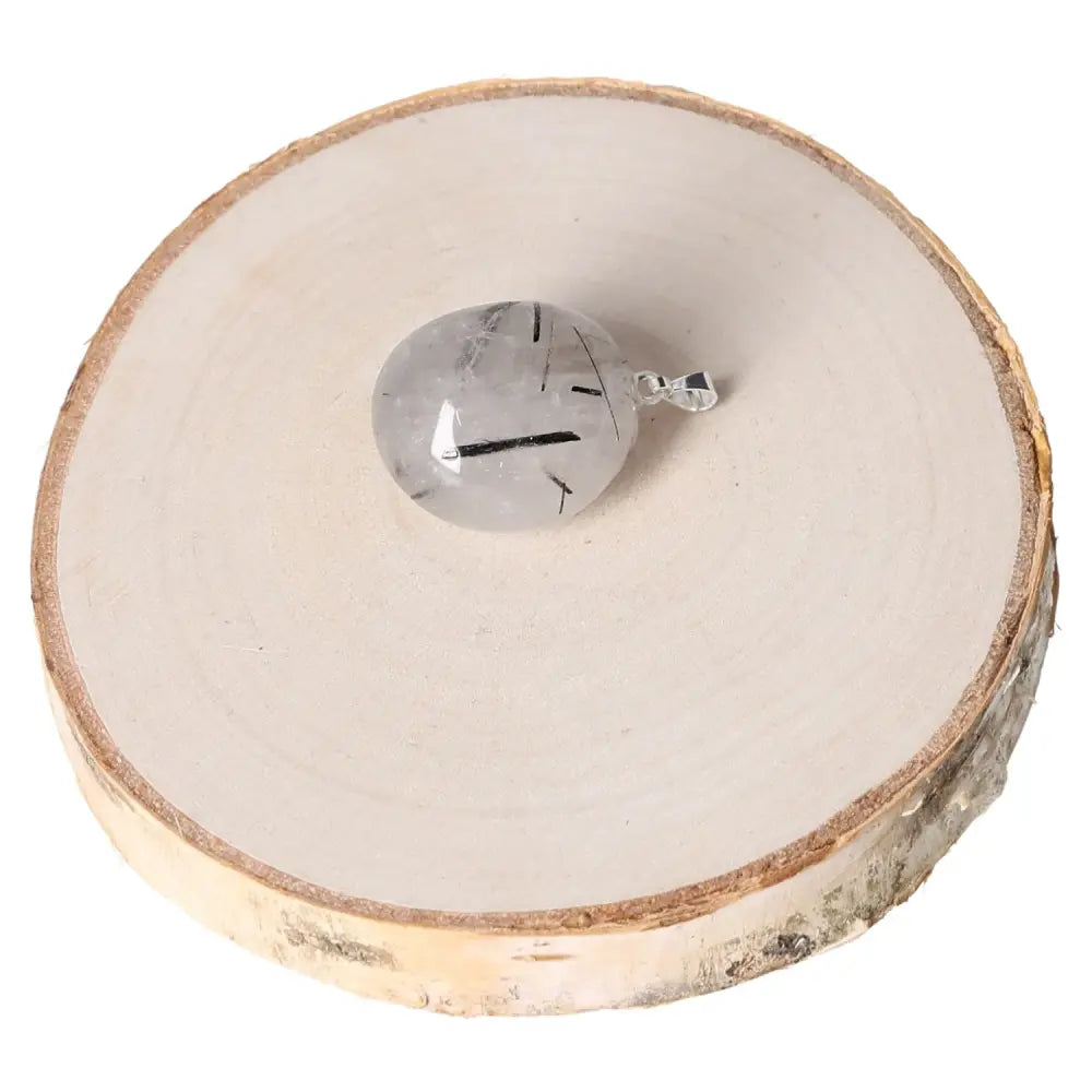 Rock Crystal with Tourmaline AA Tumbled Pendant on wooden slab, showcasing clarity and elegance.