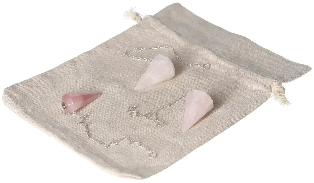 Rose Quartz pendulums on a drawstring bag, showcasing their gentle pink stone and silver chain, ideal for love and emotional healing.