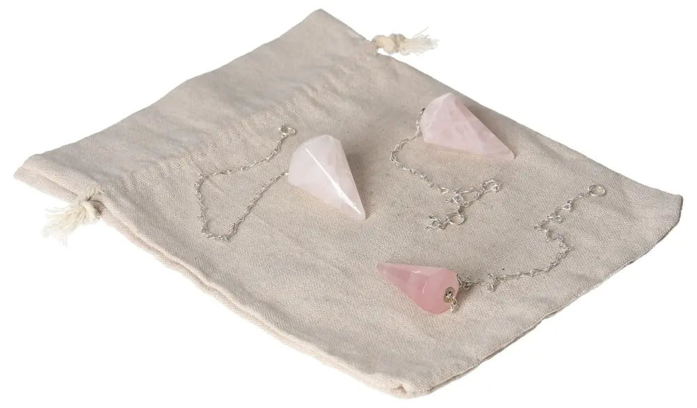 Three rose quartz pendulums on a beige cloth, symbolizing love and emotional healing.