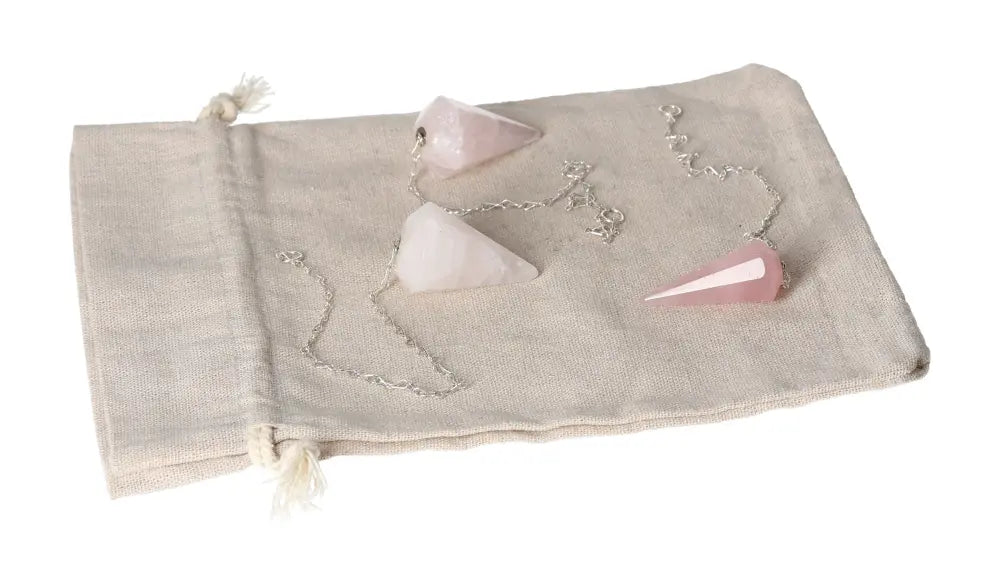 Three rose quartz pendulums on a linen pouch, symbolizing healing and love.