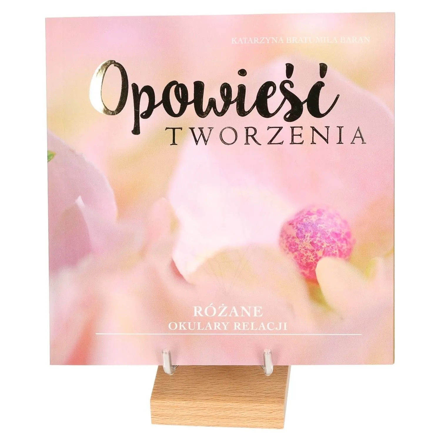 Opowieści Tworzenia book cover displayed on a stand, featuring soft pink and floral theme.