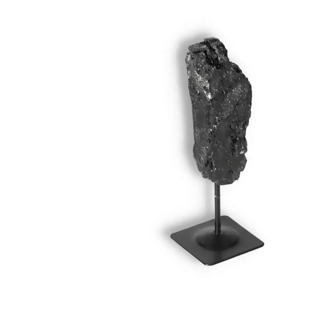 Rough black tourmaline crystal on metal stand by Sylvia Crystals, known for cleansing and transforming negative energies.