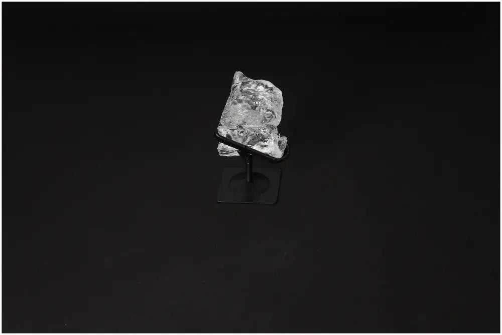 Rough clear quartz stone on metal stand against dark background showcasing crystalline structure and purification properties.