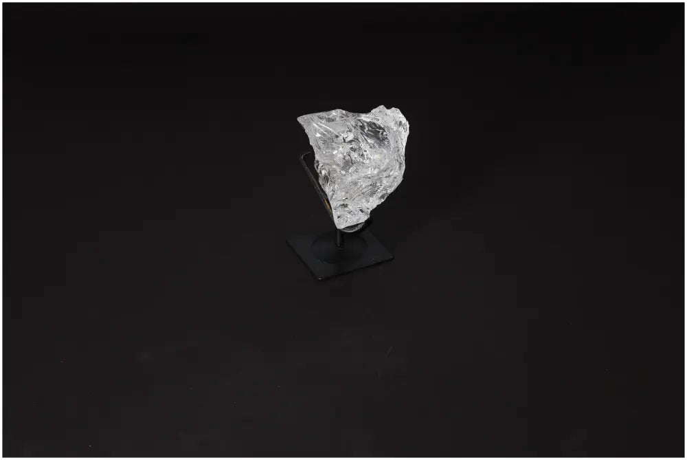 Rough clear quartz on a sleek metal stand placed against a dark background, showcasing its natural beauty and energy-cleansing properties.