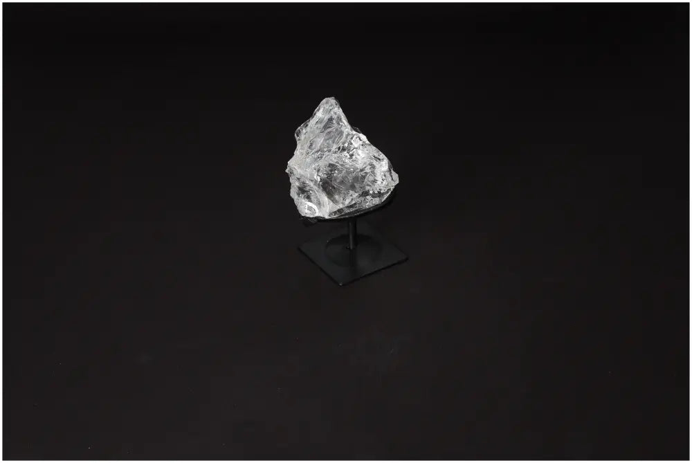 Clear Quartz crystal on metal stand, known for purification and energy harmonization, against dark background.