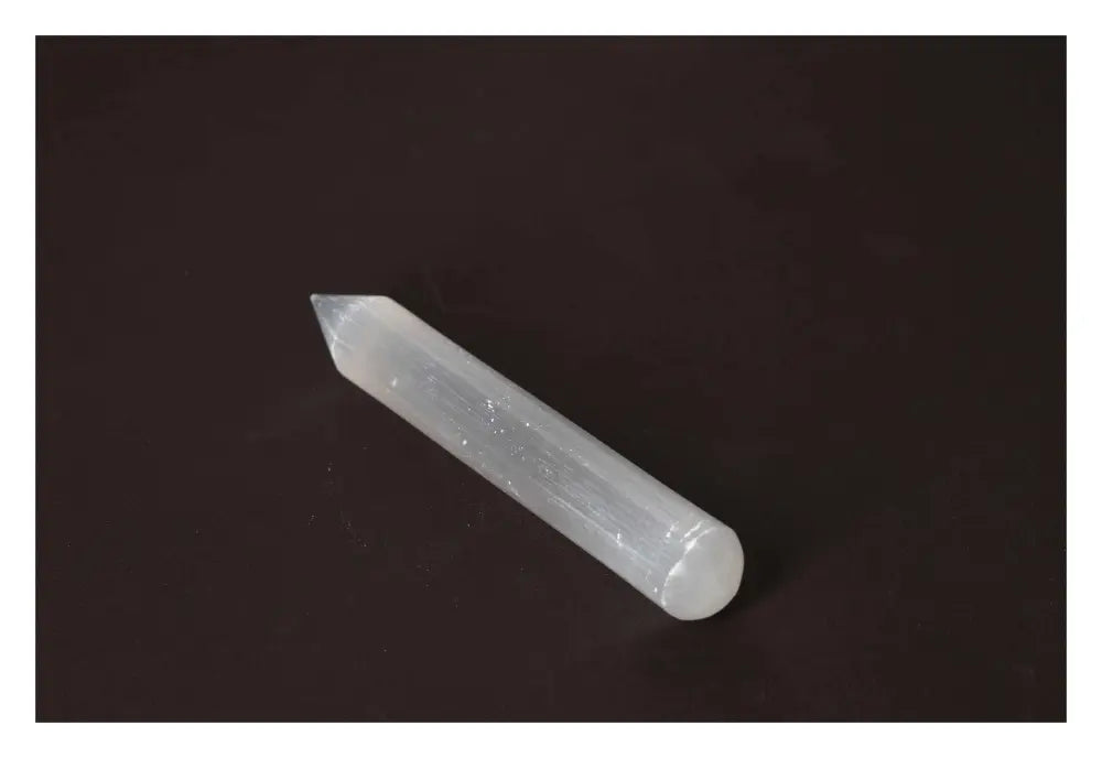 Translucent selenite massage wand on dark background, showcasing its silky texture and light-reflecting properties for calming energy.