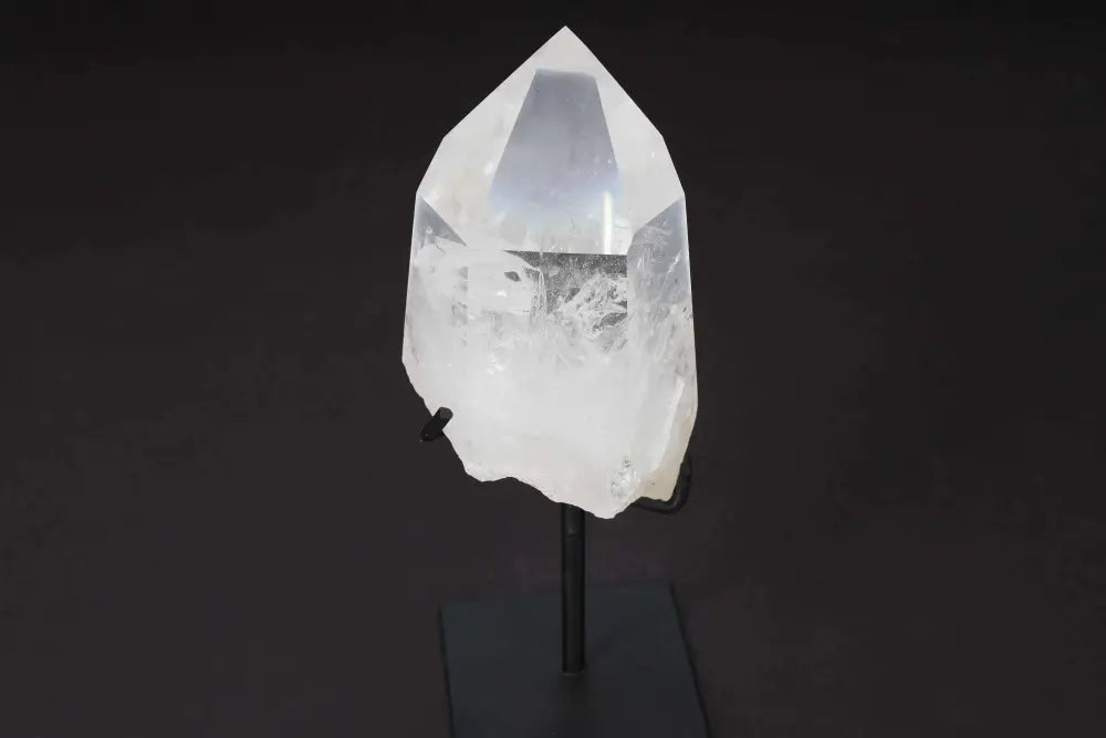 Semi Polished Clear Quartz Point with Stand, known for amplifying energy and intention, on a refined display stand against a dark background.