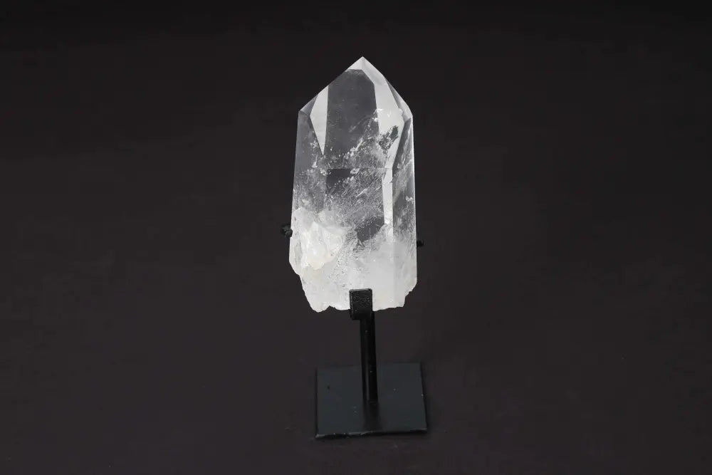 Semi polished clear quartz point with stand for energy clarity and alignment on a black background.