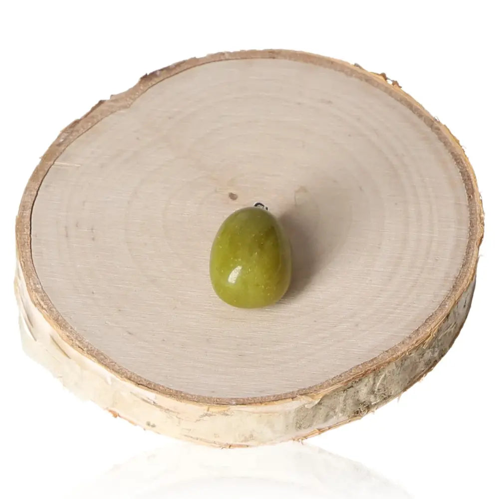 Serpentine/Lizardite tumbled pendant displayed on a wooden slab, showcasing its unique green hues and mystical allure.