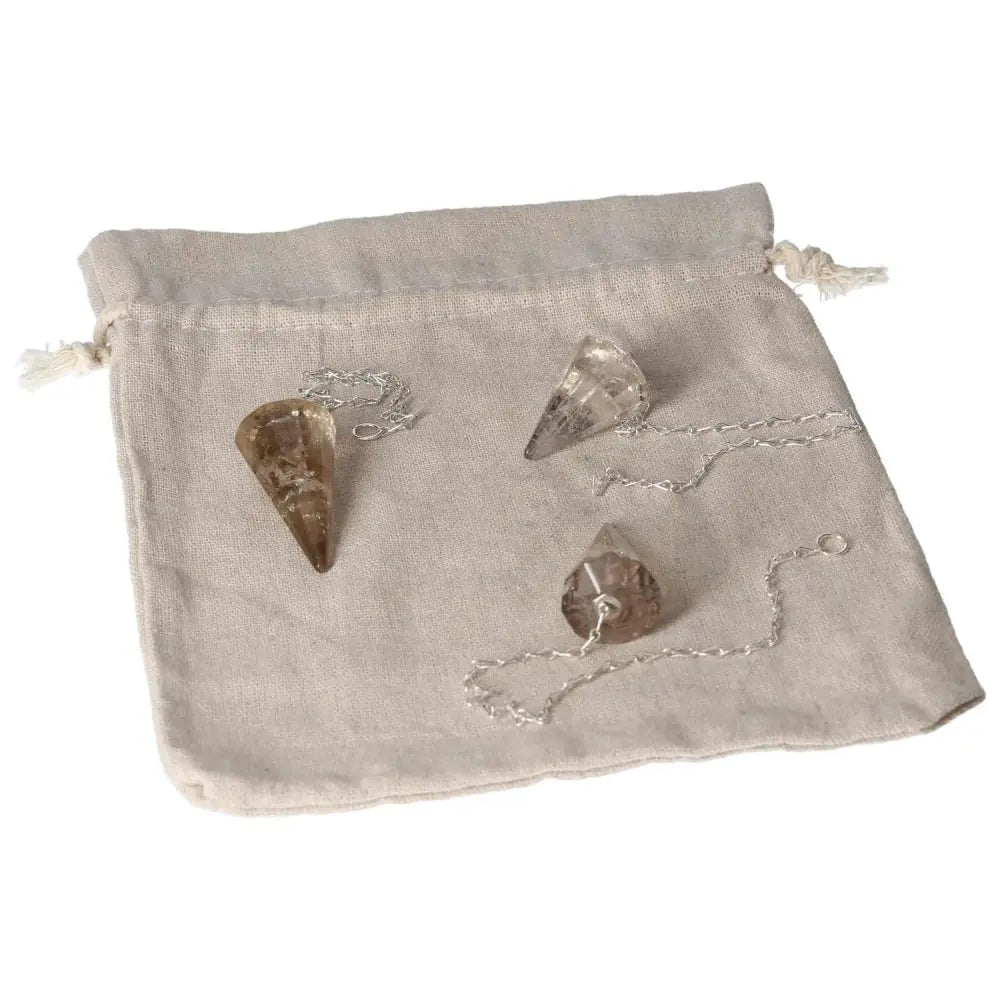 Set of three smoky quartz pendulums with silver chains on a beige drawstring pouch, ideal for grounding and decision-making.