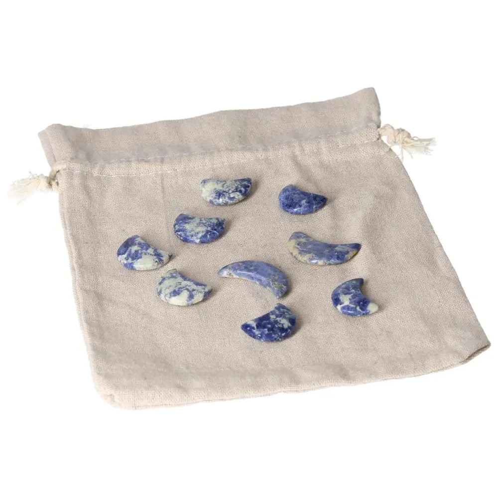 Collection of small Sodalite crescent moons with indigo tones and white marbling placed on a beige cloth pouch for intuition and calm.