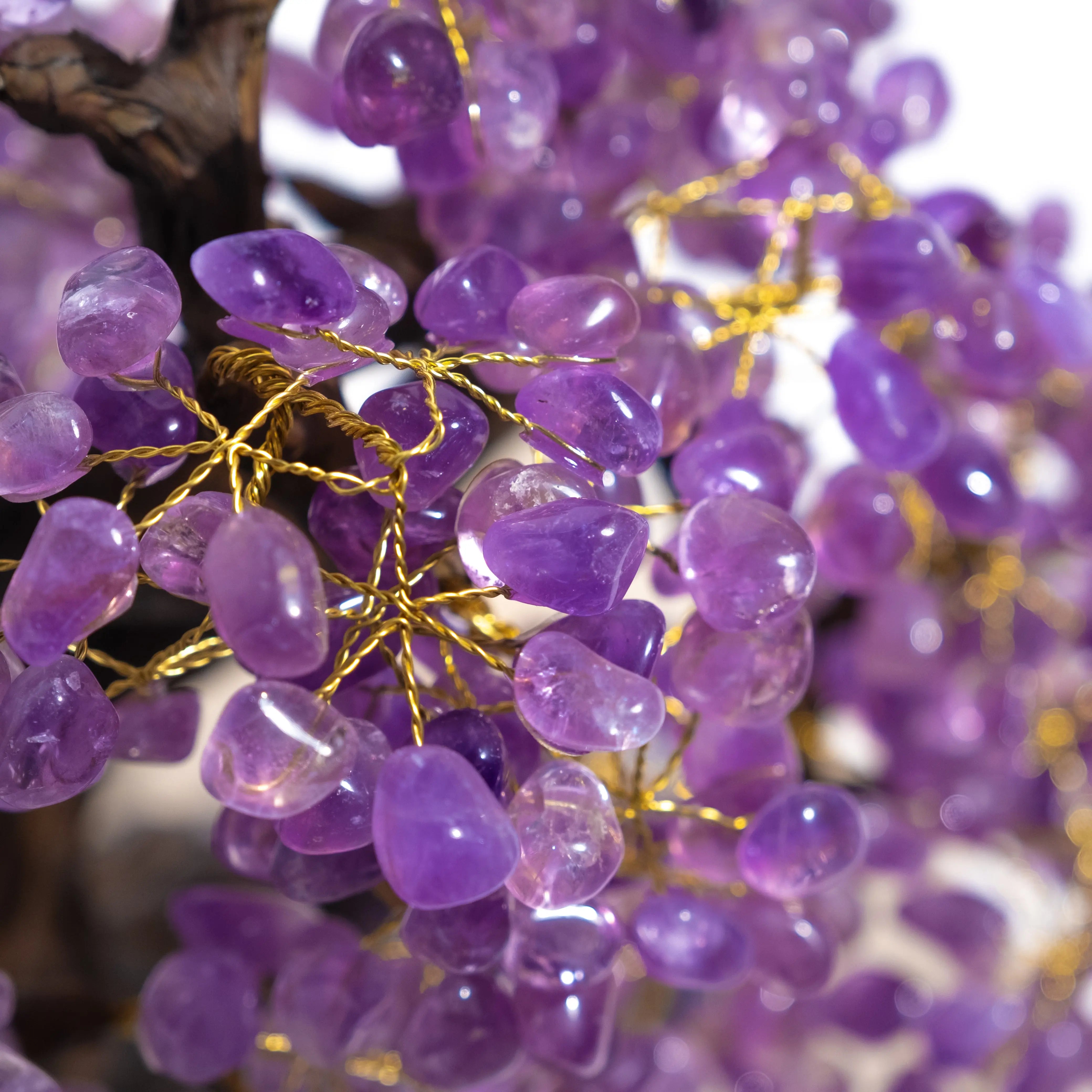 Close-up of a handcrafted amethyst crystal bonsai tree with purple gemstone leaves on gold wires, promoting spiritual harmony.