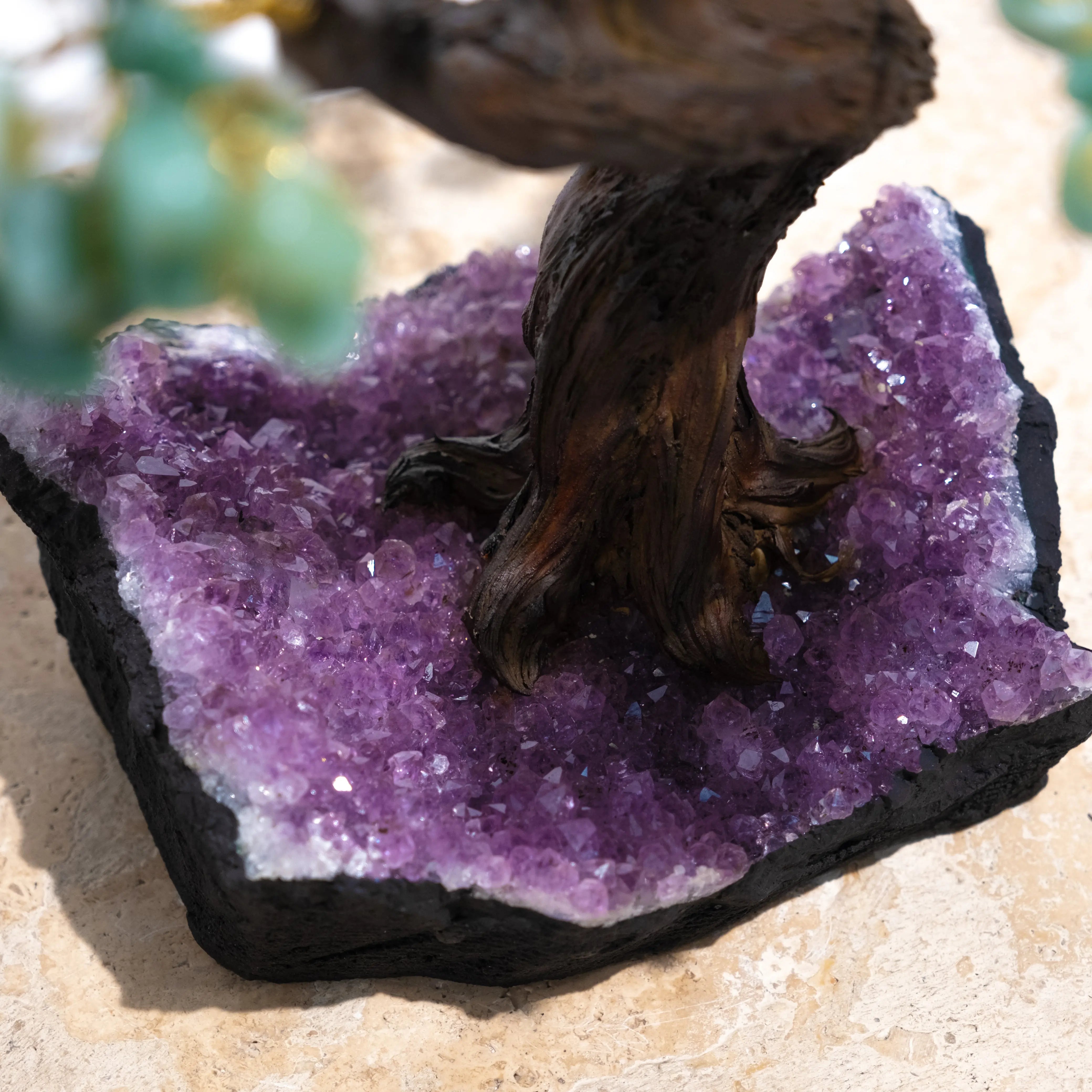 Base of a tumbled aventurine bonsai tree on amethyst crystal cluster surface, enhancing prosperity and positive energy.