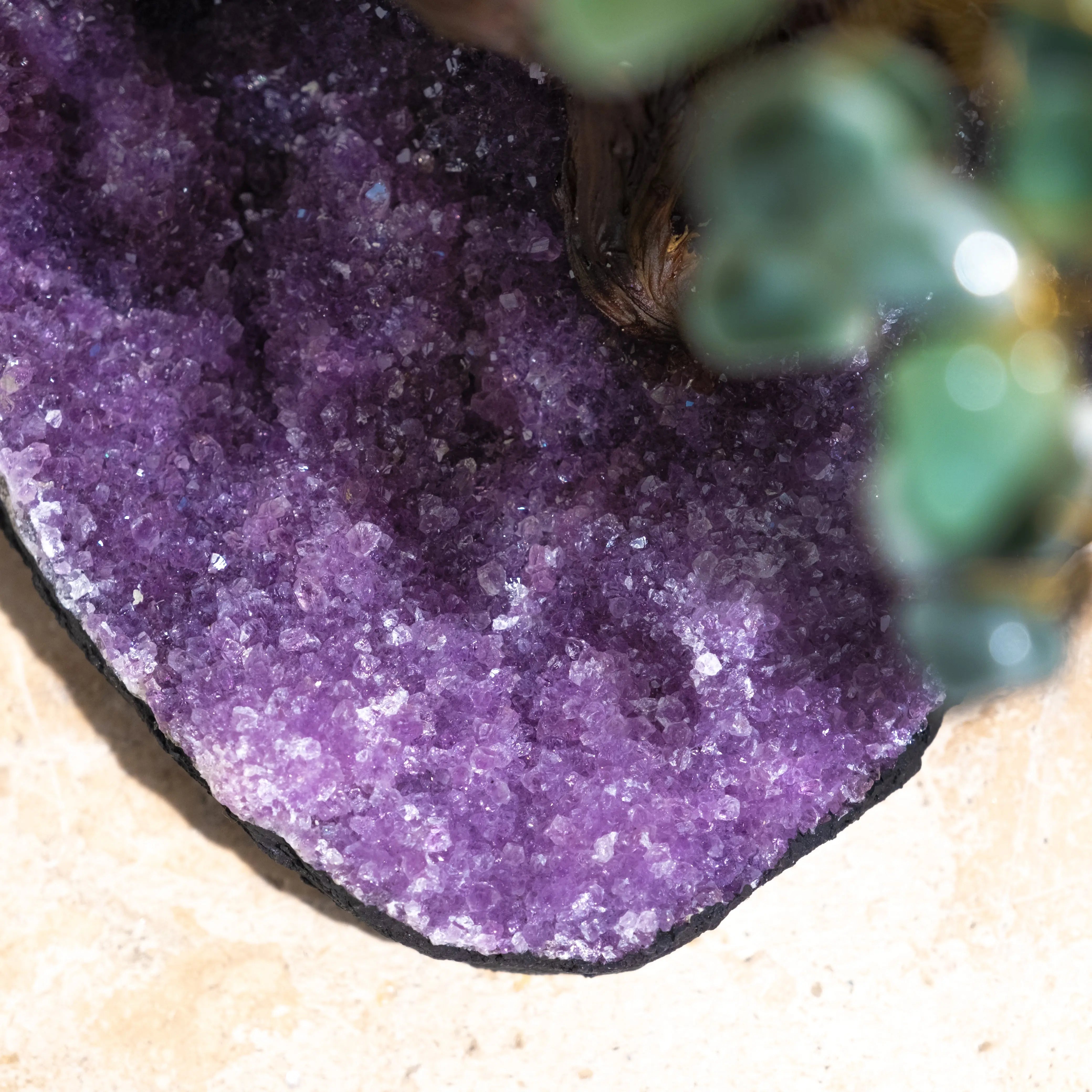 Close-up of purple crystal base of Aventurine Bonsai Tree, showcasing its sparkling texture and contrast with green leaves.