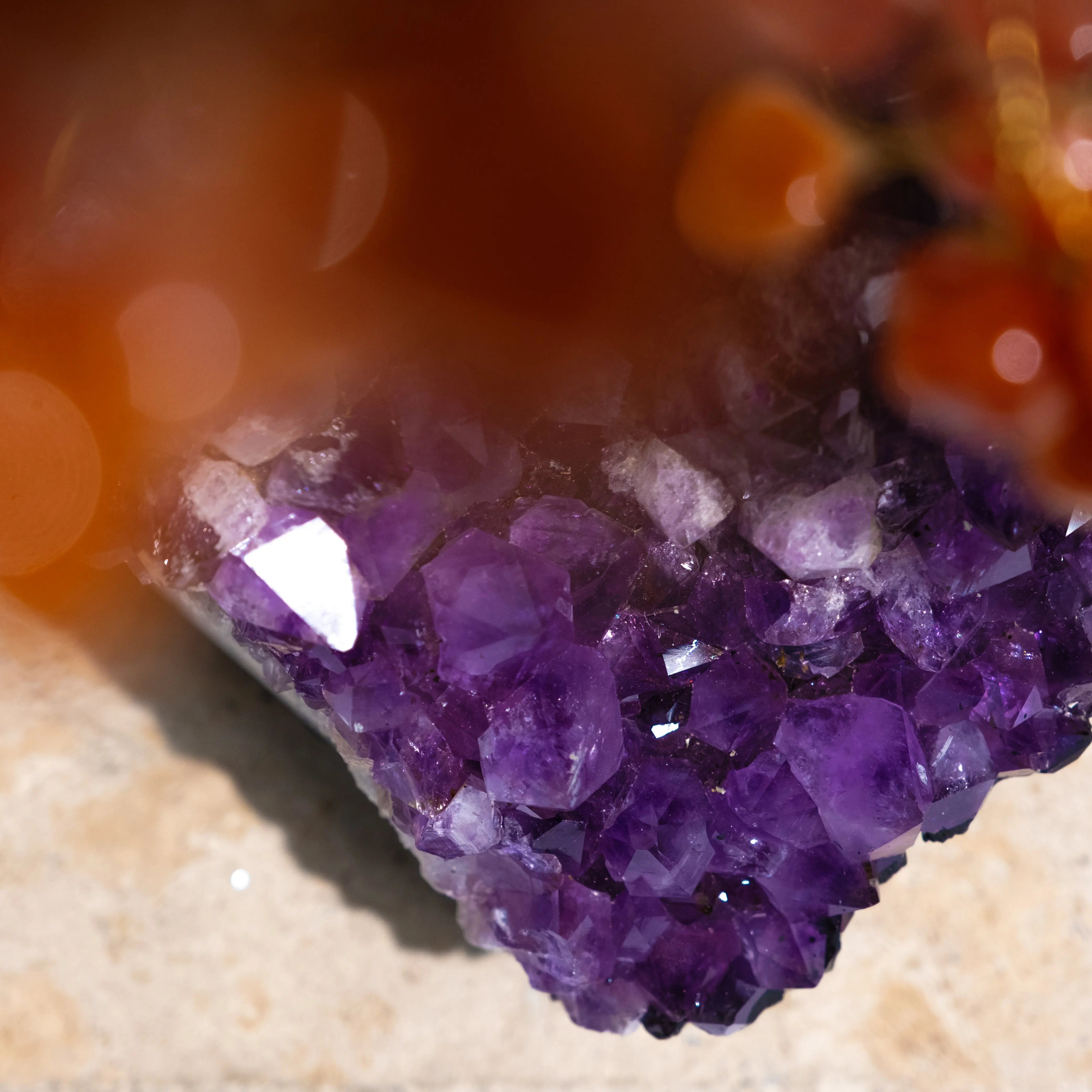 Close-up of a vibrant purple gemstone crystal with an orange hue in the foreground, highlighting the intricate facets and sparkling texture.