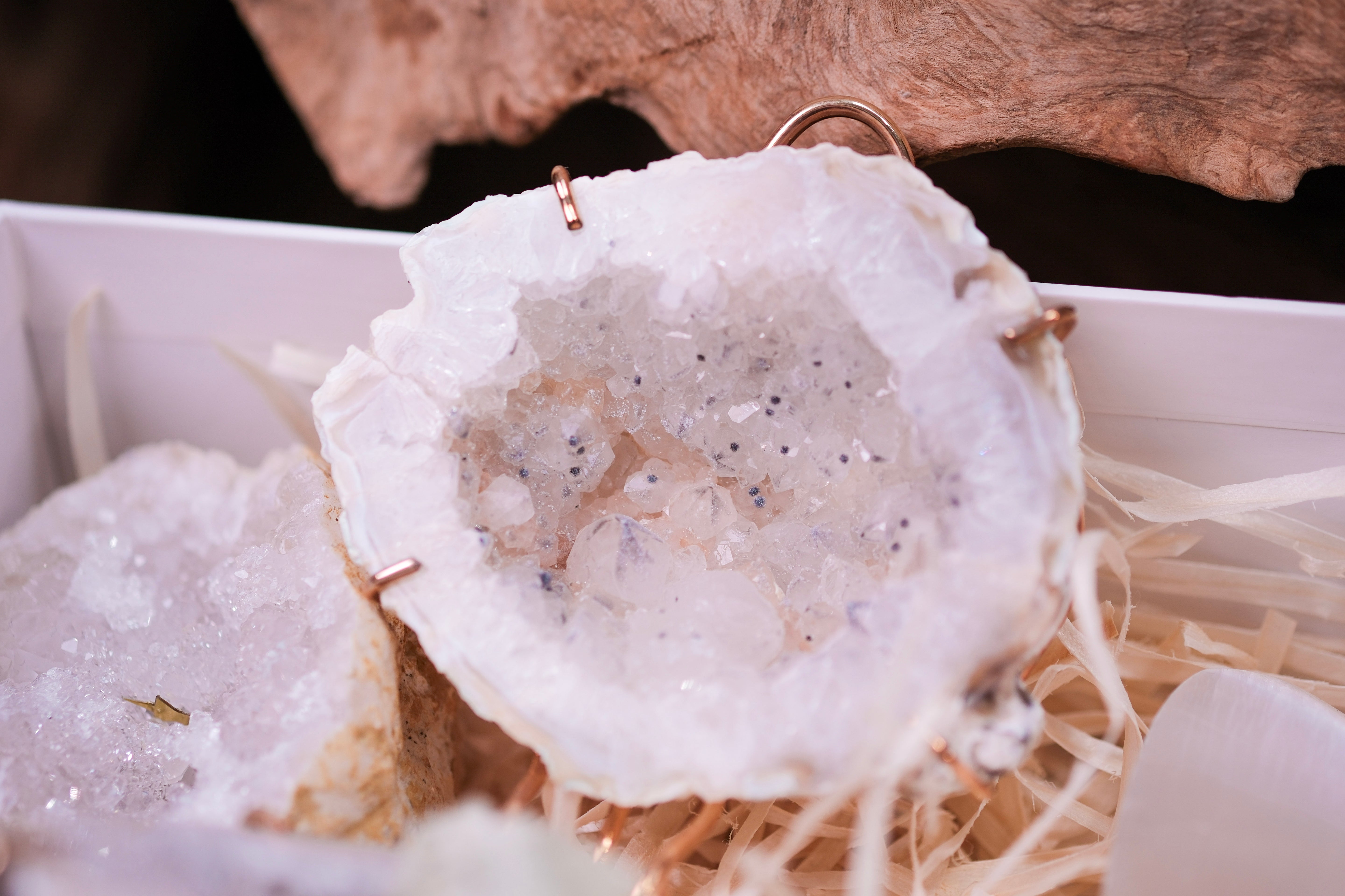 Crystal geode with sparkling white and beige tones, displayed on natural straw bedding for a rustic and elegant presentation.