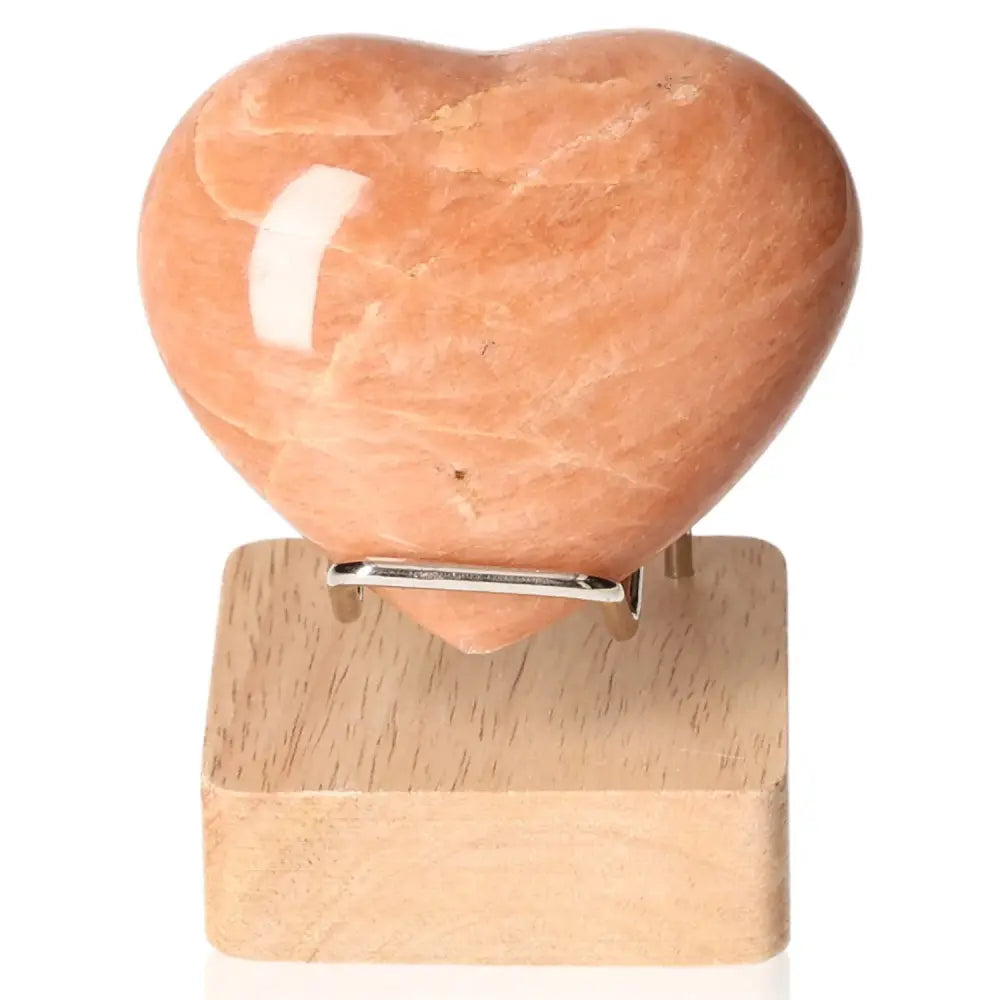 Peach Moonstone Heart crystal on wooden stand, symbolizing emotional balance and intuition, promotes restful sleep and emotional depth.