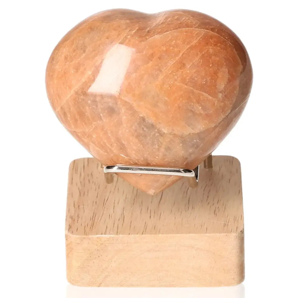 Peach Moonstone Heart enhancing emotional balance and intuition, shown on a wooden stand. Stand not included.
