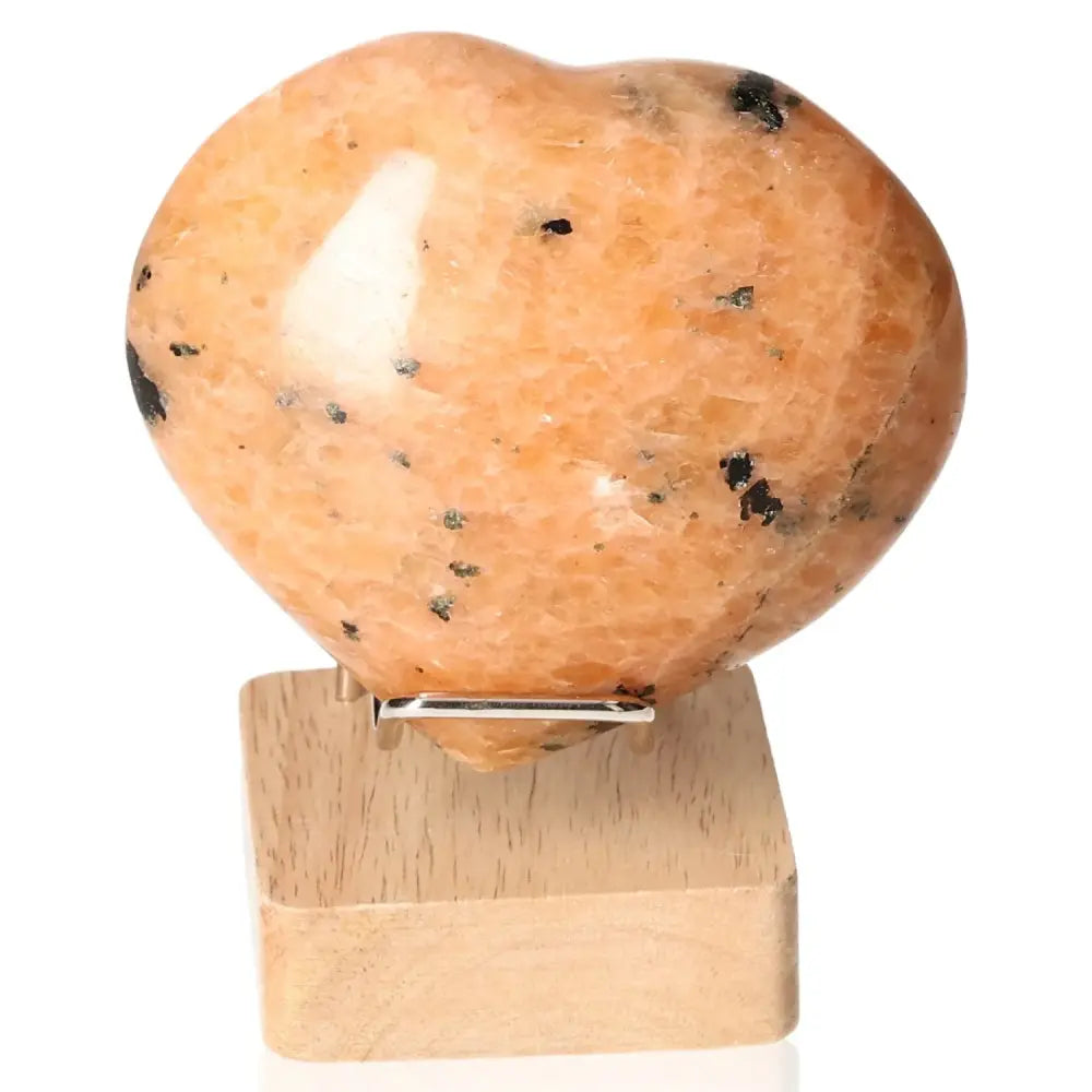 Peach Moonstone Heart crystal promoting emotional balance, intuition, and protection from nightmares on a wooden stand.