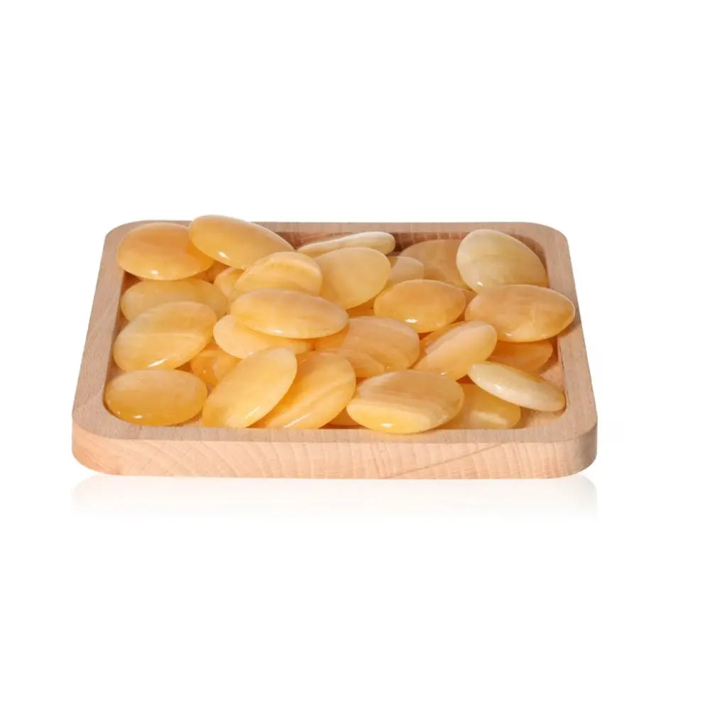 Yellow Calcite Palm Stones on wooden tray promoting self-confidence, motivation, energy, and learning benefits.