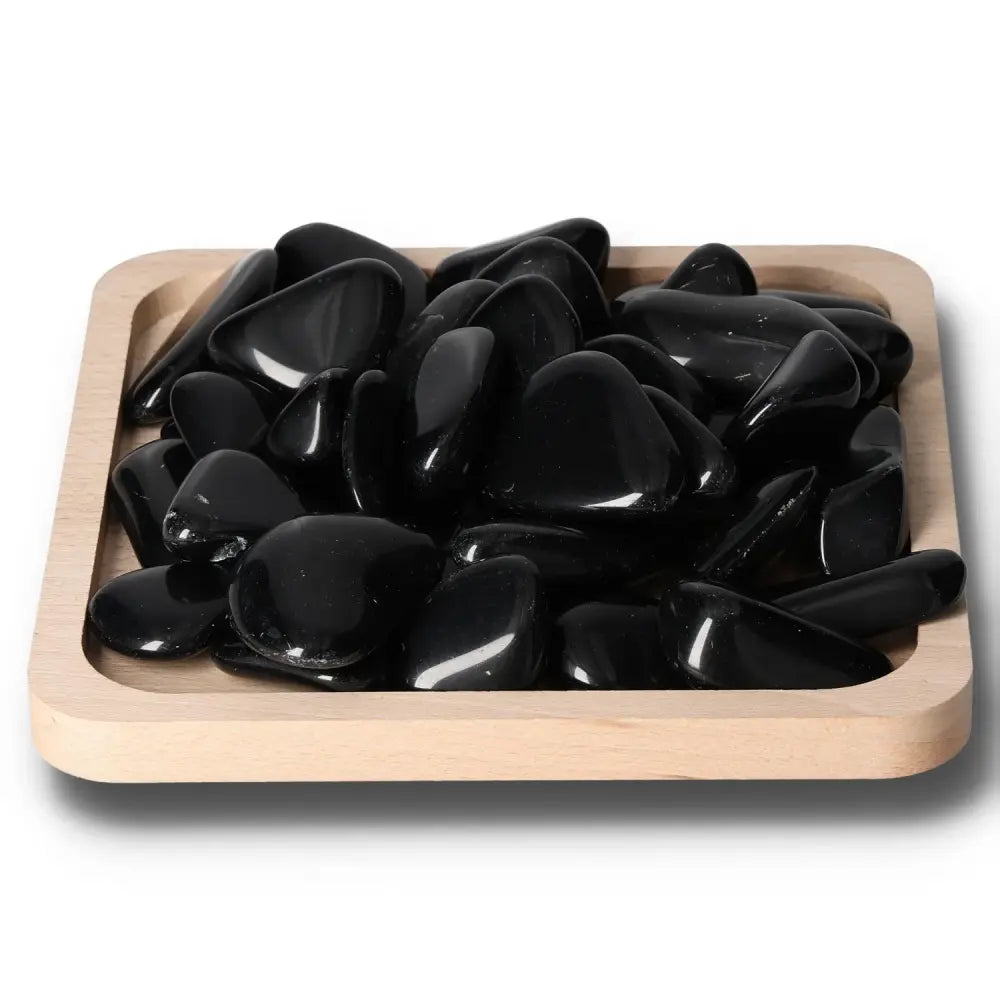 Tumbled Obsidian stones on a wooden tray, known for protective energy and absorbing negativity, creating a serene environment.