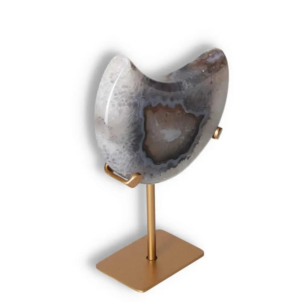 Agate lunar crescent with natural geode, featuring off-white swirls on a gold stand, illuminating your space with celestial elegance.