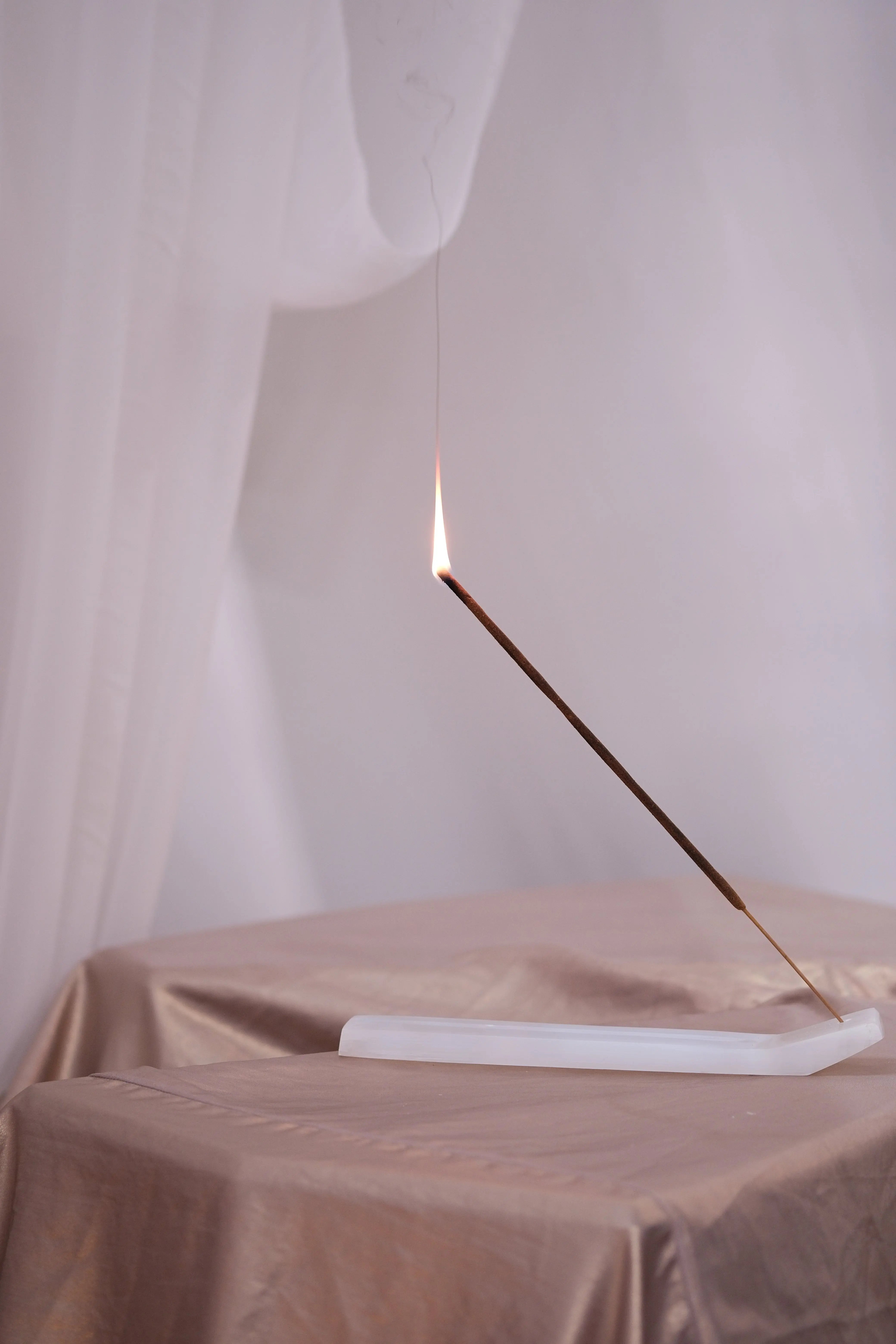 Lit incense stick on table, Bali Harmony Abundance blend, emits soothing aroma for balance and serenity.