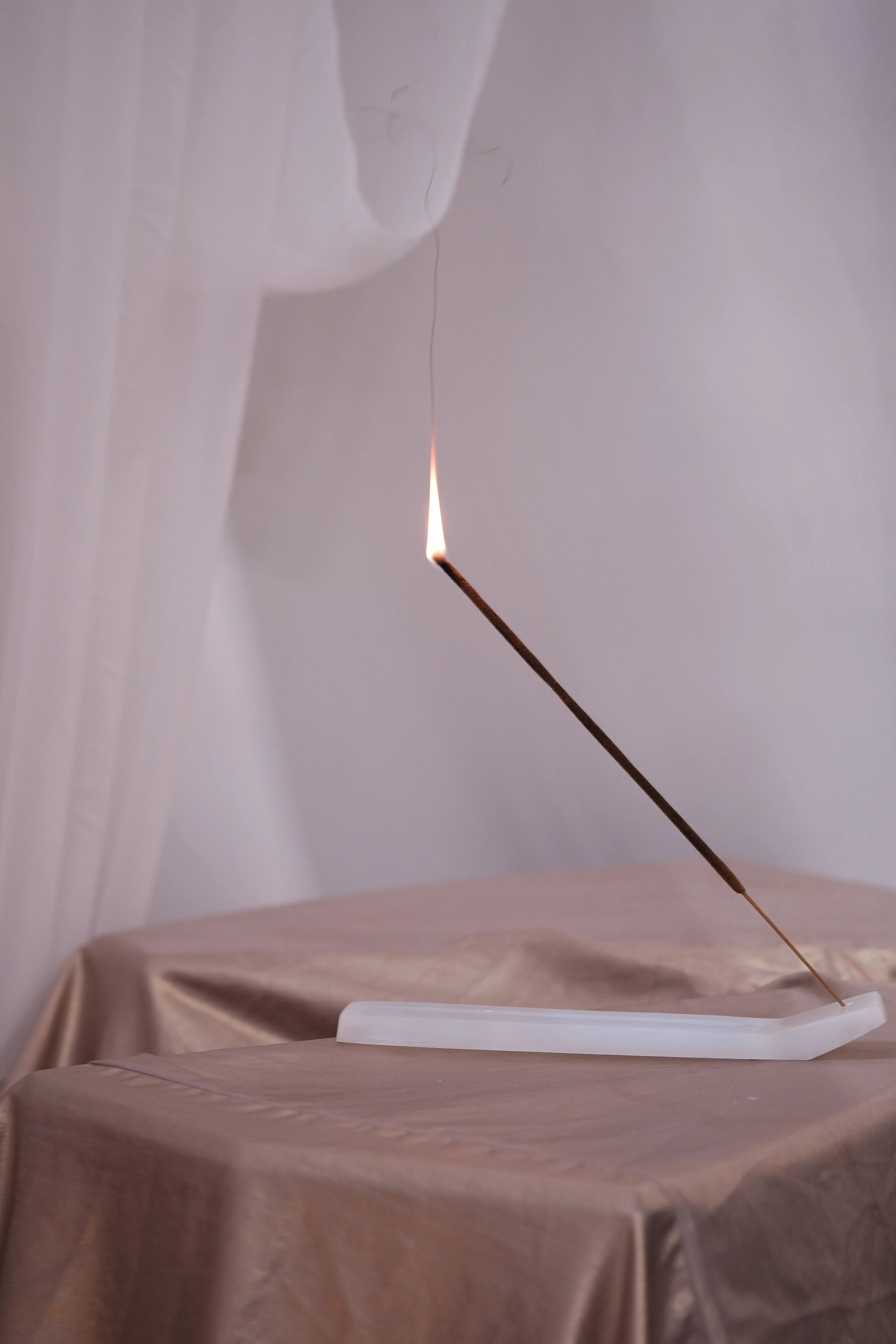 Lit incense stick on a white holder, evoking Bali Harmony with serene ambiance.