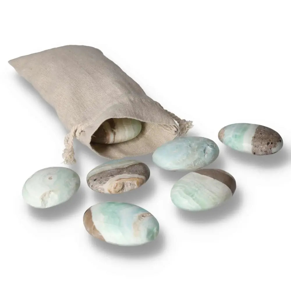 Caribbean Calcite palm stones spilling from a burlap bag, displaying soothing blue and creamy white hues, from Sylvia Crystals.