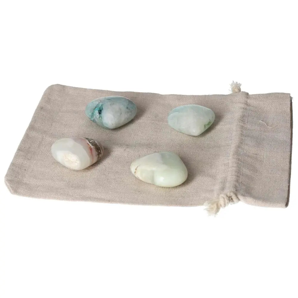 Four Chrysocolla heart-shaped stones on a beige pouch, promoting communication and emotional balance with feminine energy.