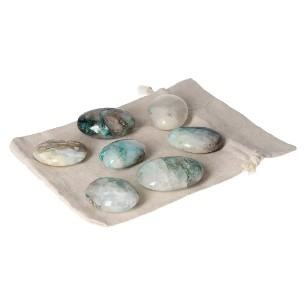 Collection of chrysocolla palmstones on a beige pouch, showcasing their natural blue-green hues.