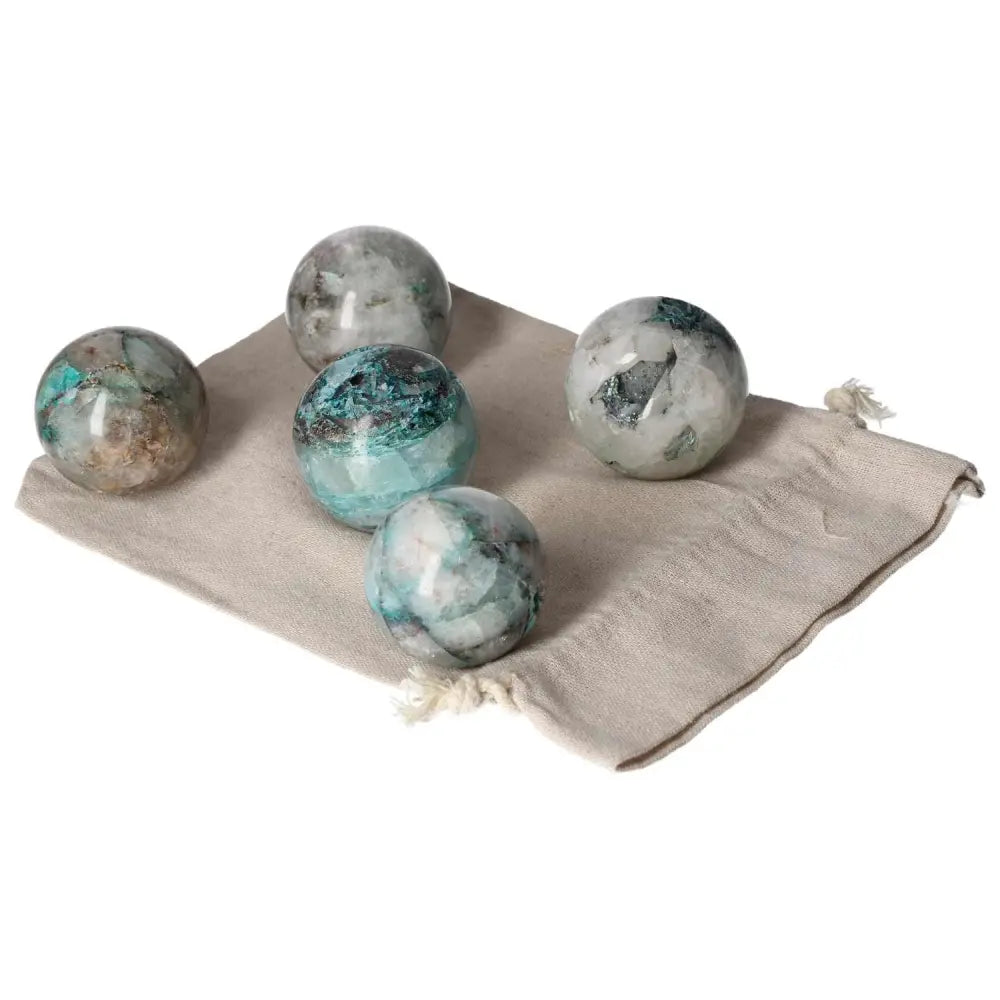 Five chrysocolla spheres displayed on a beige fabric pouch, showcasing their unique blue-green patterns and polished surfaces.