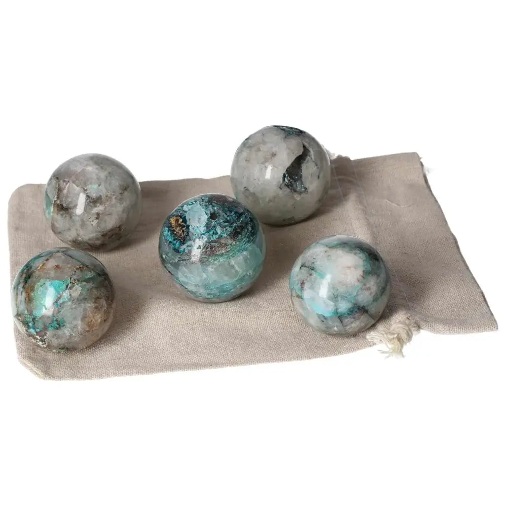 Five chrysocolla spheres on a beige fabric, showcasing blue-green hues and natural patterns.