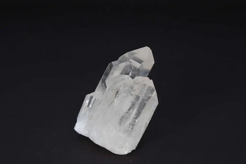 Clear quartz cluster with multiple crystal points on dark background, amplifying energy and purifying space.