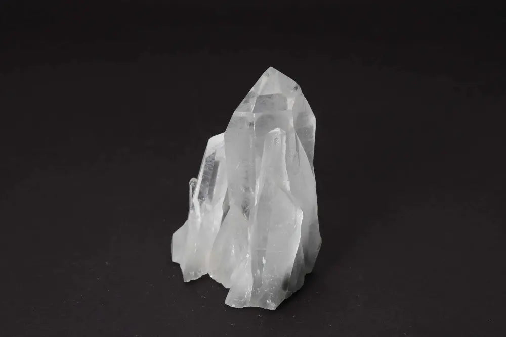 Clear quartz cluster with multiple crystal points on dark background, radiating high vibrational energy to cleanse and harmonize spaces.