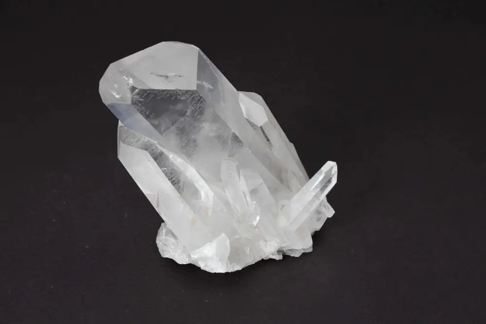 Clear quartz cluster crystal on black background, showcasing multiple points and high vibrational energy for cleansing and harmony.