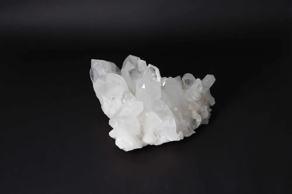 Clear Quartz Cluster on dark background radiating high vibrational energy, with multiple crystal points for amplifying intention and harmony.