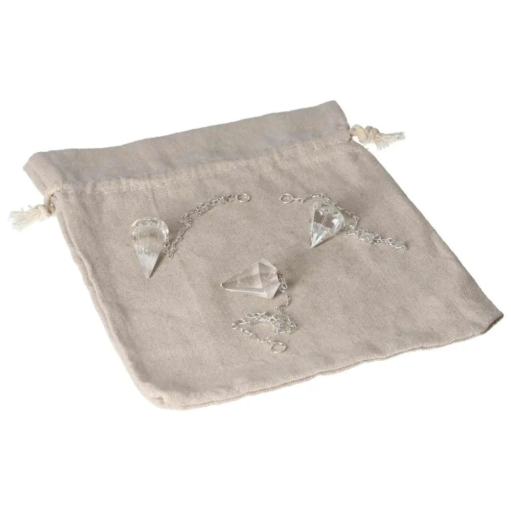 Clear Quartz Pendulums with chains on a beige drawstring bag, known for purification and harmonizing the body and mind.