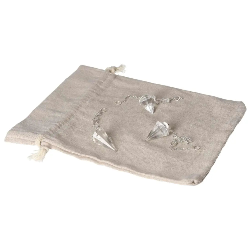 Clear Quartz pendulums on a beige fabric pouch, ideal for energy purification and harmonizing negative vibrations.
