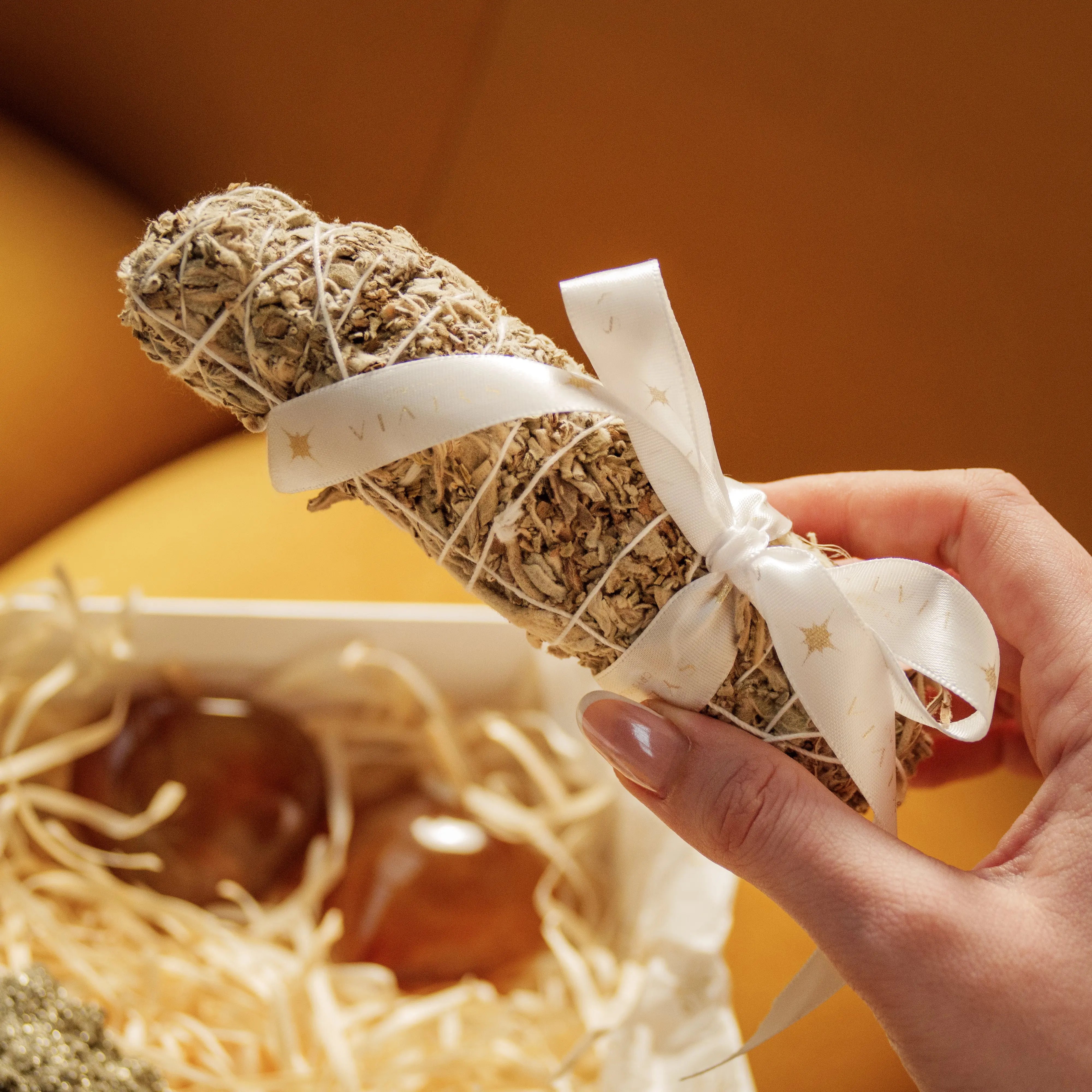 Hand holding white sage bundle above Eternal Love Gift Box with Carnelian Hearts and Rough Pyrite for Valentine's Day