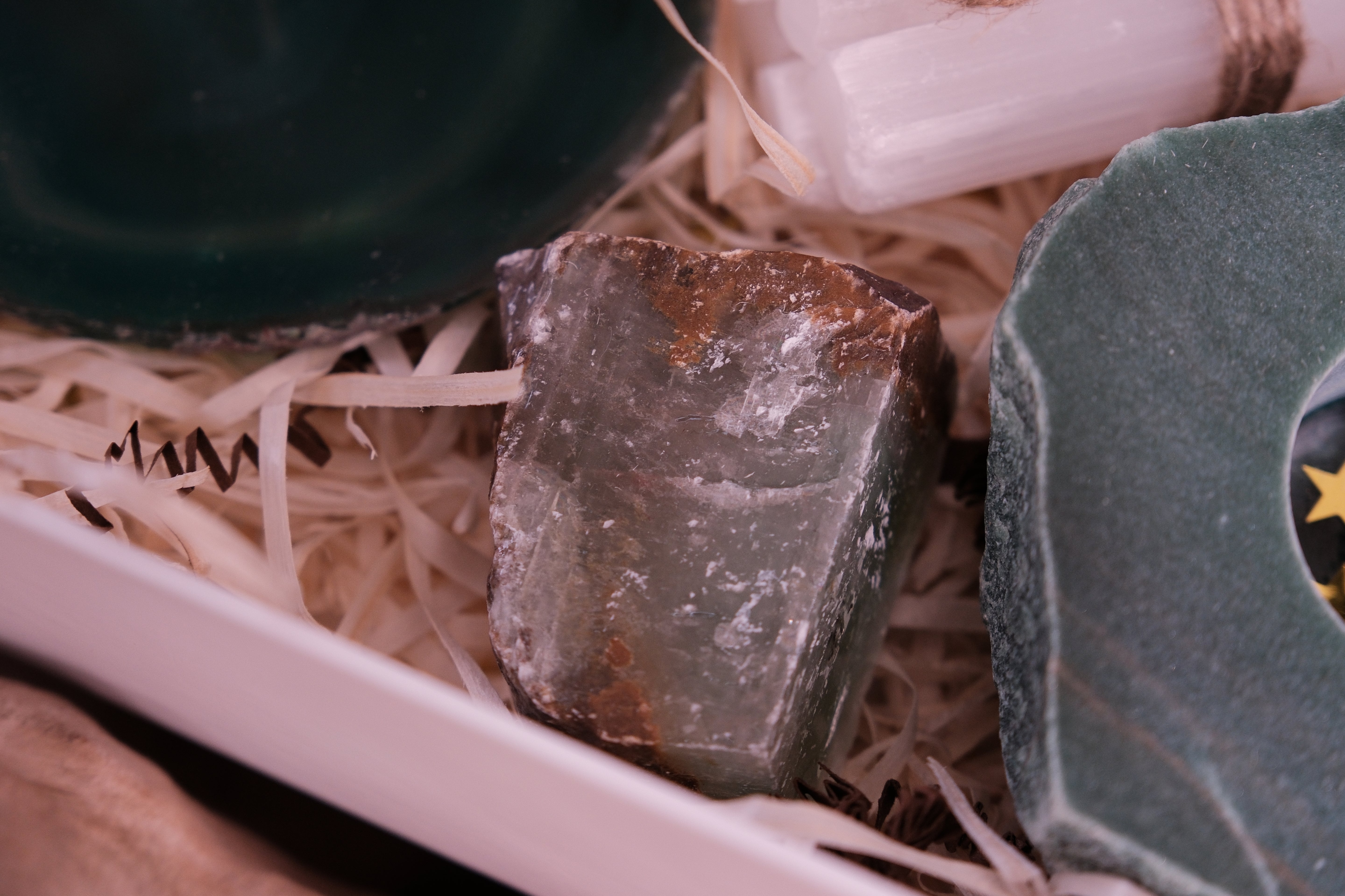 Close-up of crystals in the Sylvia Crystals Christmas Gift Box for balance and tranquility, featuring green stones on straw bedding.