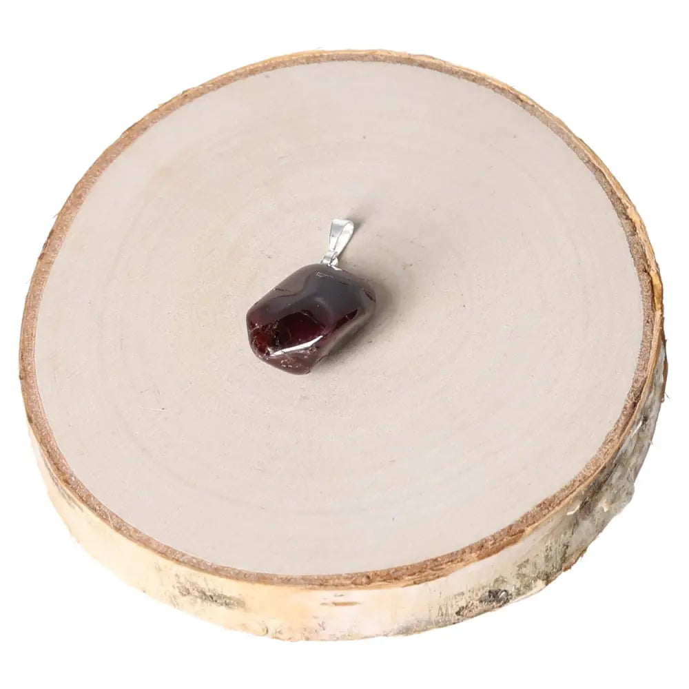 Garnet AA Tumbled Pendant featuring a rich, deep red gemstone with a smooth texture on a wooden display, showcasing elegant jewelry design.