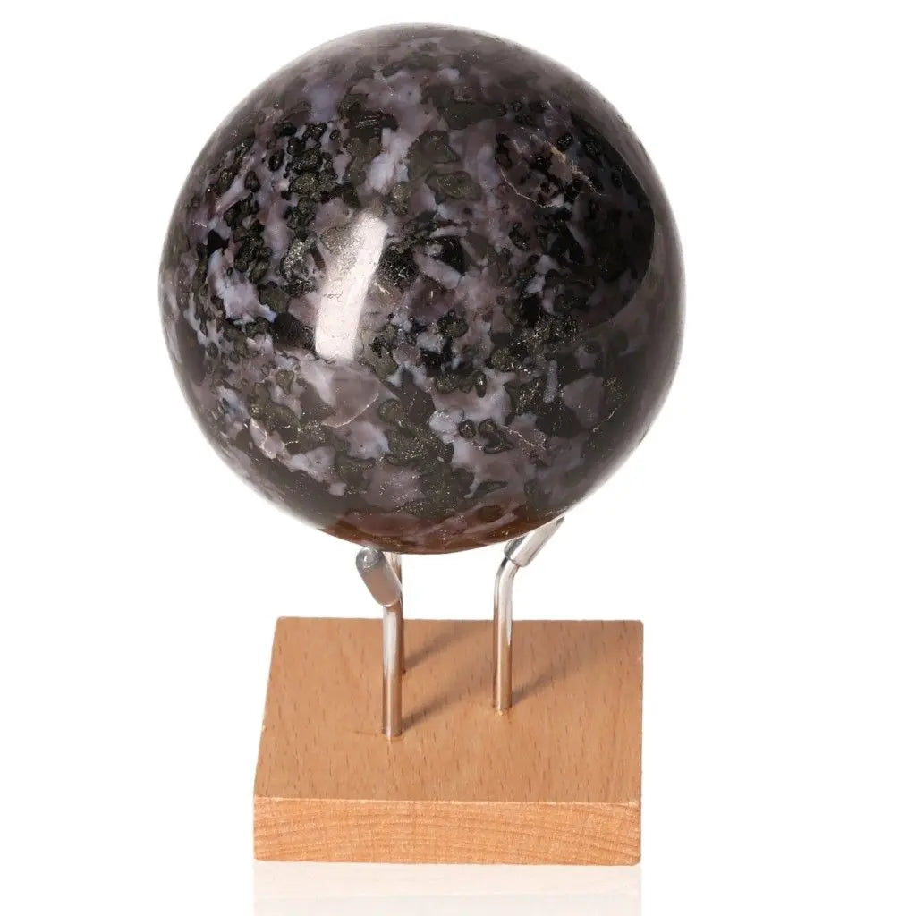 Indigo Gabbro Sphere with mystical black and indigo patterns, known for enhancing intuition and spiritual growth, displayed on a wooden stand.