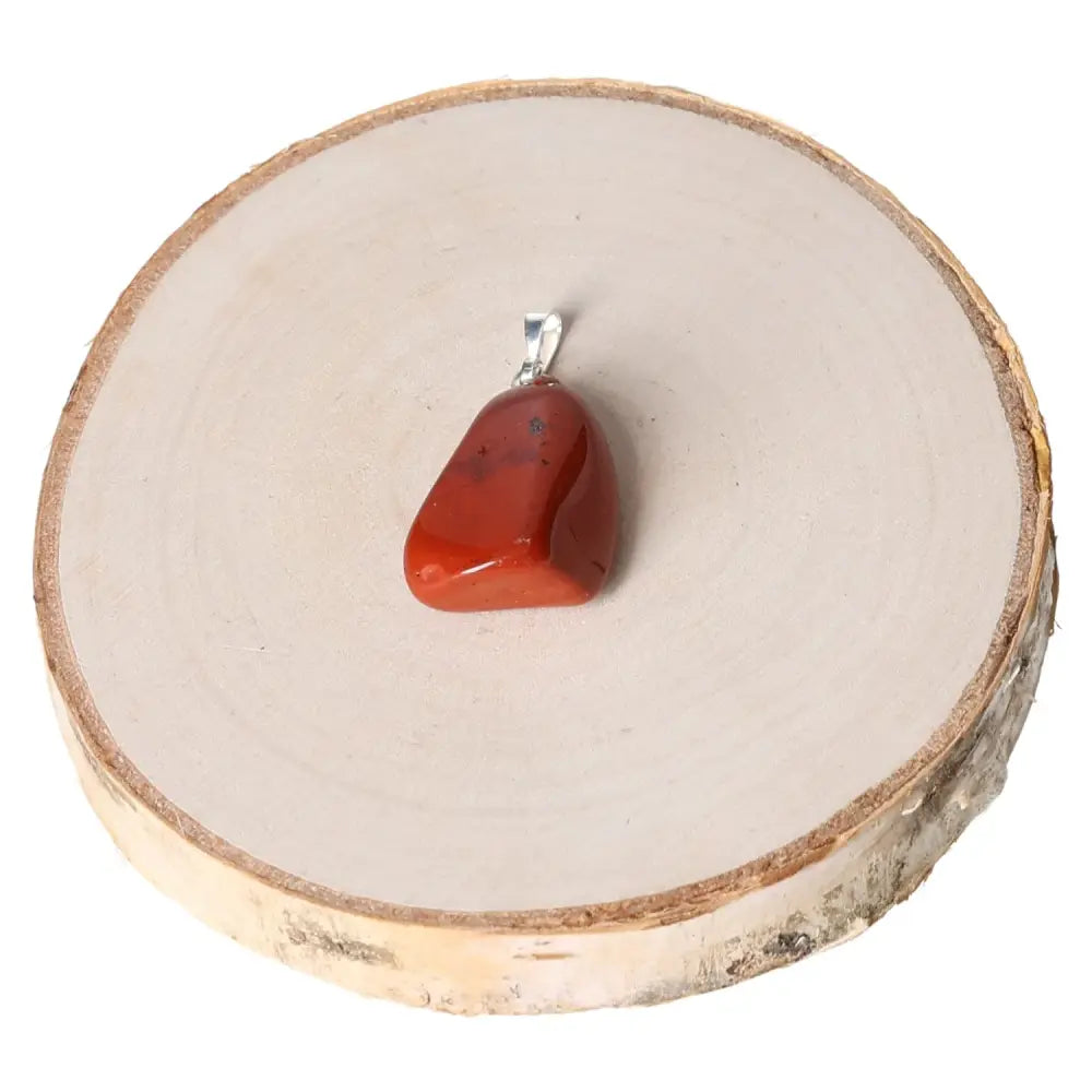 Jasper Red Tumbled Pendant on wooden stand, showcasing vibrant colors and smooth finish, symbolizes strength and elegance.