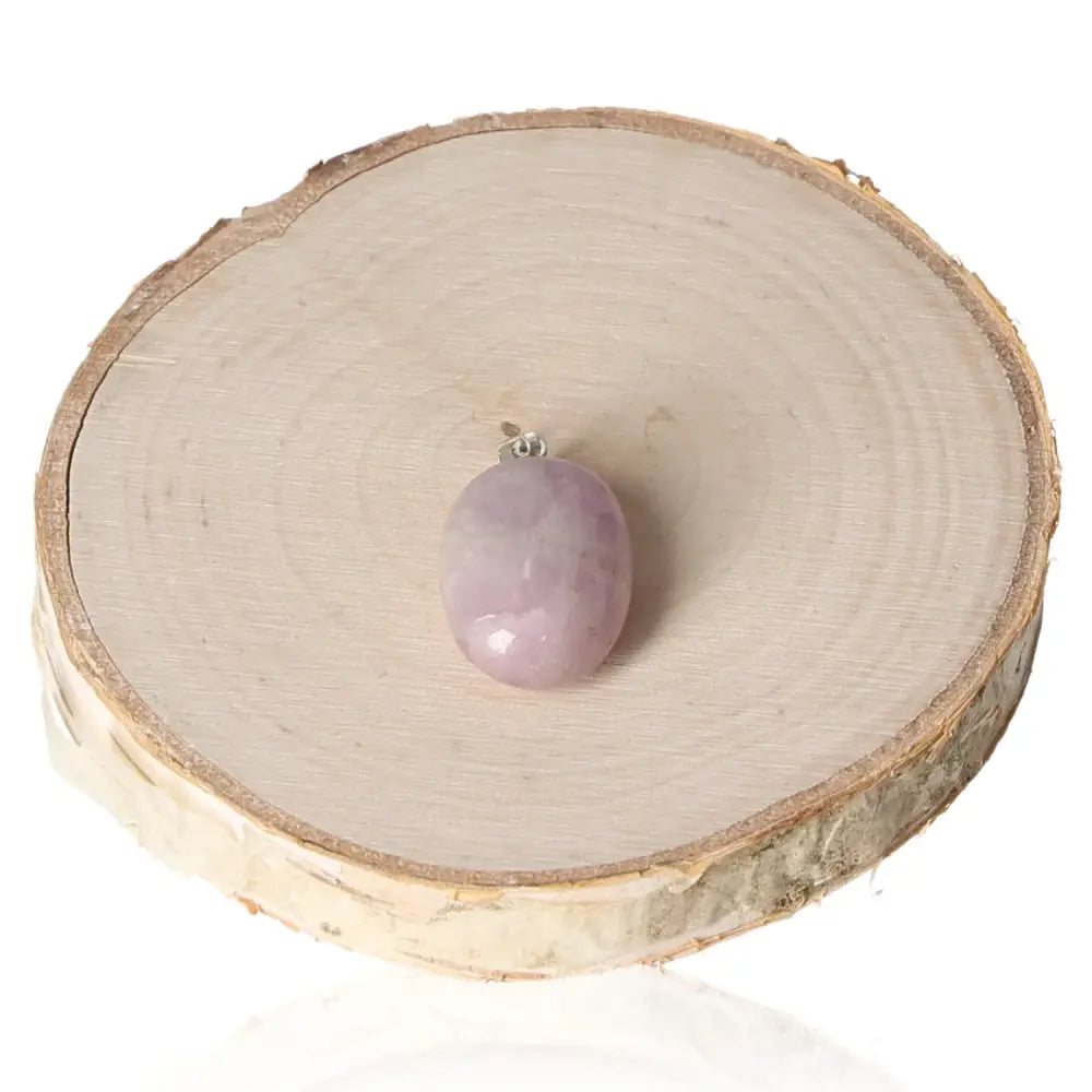 Kunzite Tumbled Pendant with soft pink-lavender hues on wooden display, offering soothing energy and elegance.