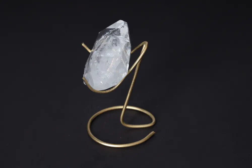 Clear Quartz crystal displayed on a gold stand, showcasing its geometric elegance and purity against a dark background.