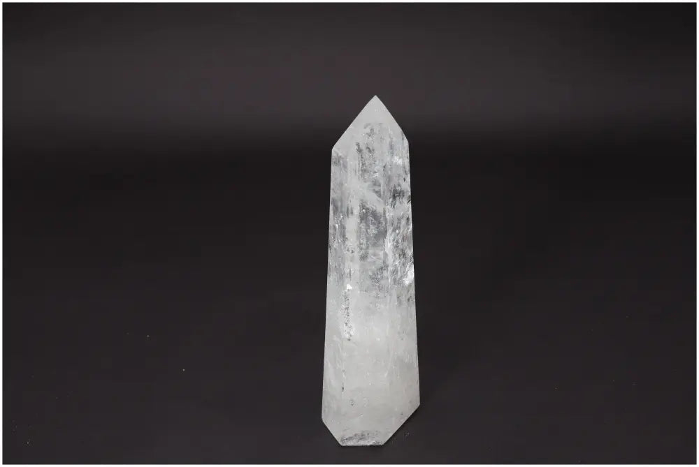 Lemurian Quartz Obelisk, clear crystal standing, promoting clarity and personal growth, against a dark background.