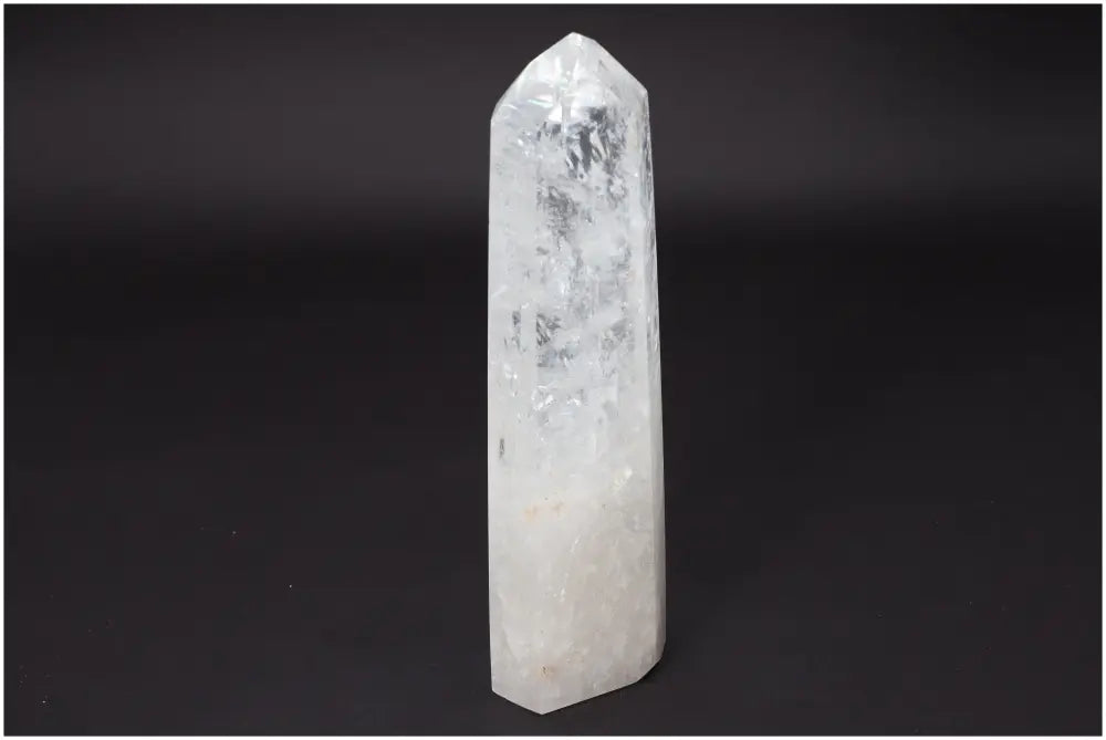 Lemurian Quartz Obelisk crystal, clear and elongated, standing upright against a dark background, symbolizing clarity and balance.