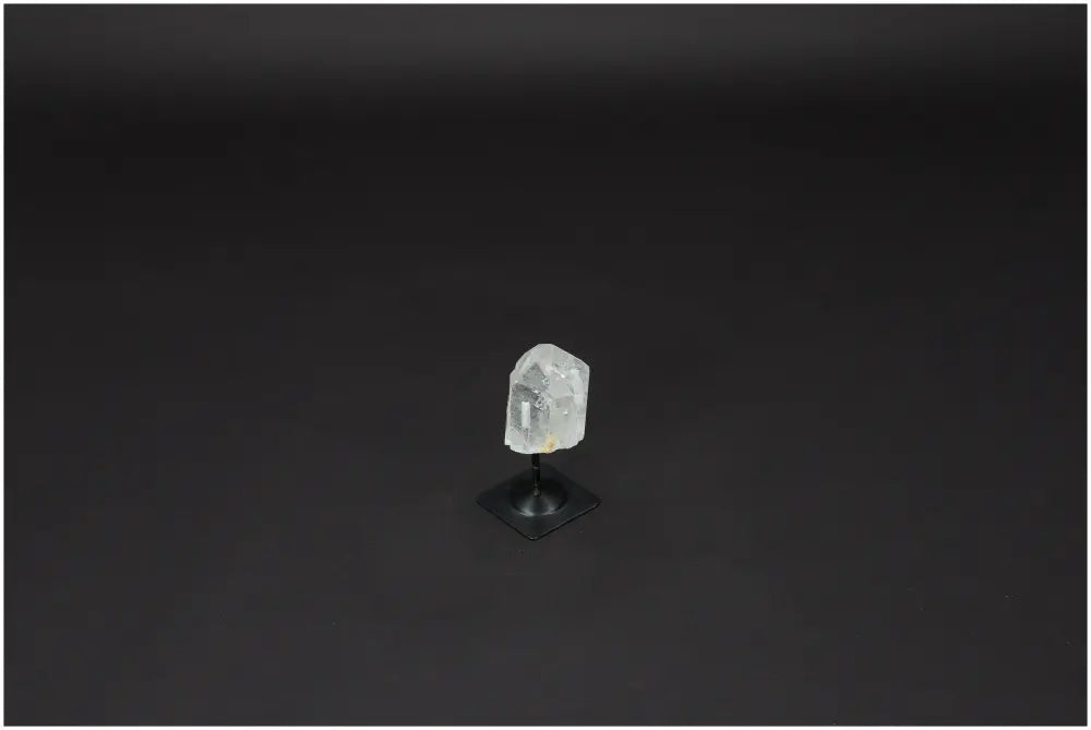 Lemurian Quartz Crystal on sleek metal stand, known for its purification and energy harmonizing properties, displayed against black background.